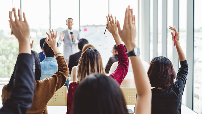 A full class of students with their hands raised